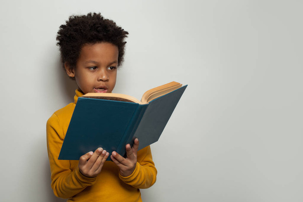 Portrait of little black child boy reading a book on white background - Foto, imagen