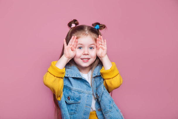 Funny little girl fooling around and makes a face on pink background - Foto, imagen