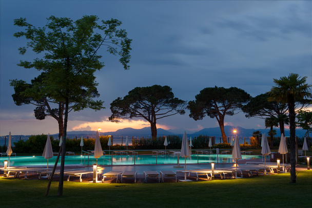 Puut uima-altaalla auringonlaskun aikaan loungereilla
 - Valokuva, kuva