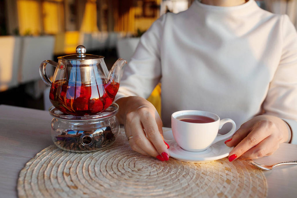 Glass teapot with  tea at cafe. Woman hands with tea cup on background - Photo, Image