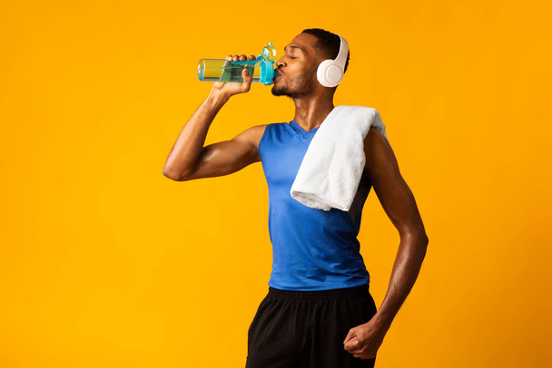 Afro sportsman drinking water listening to favourite music - 写真・画像
