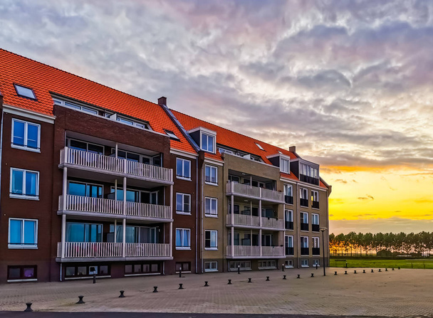 apartamentos edifício com a rua durante o pôr do sol em Sint Annaland, cidade turística em zeeland, Países Baixos
 - Foto, Imagem