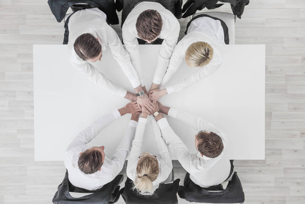 Liikemiehet joukkue pinoaa kädet istuu valkoinen konferenssi pöytä toimistossa yhtenäisyys yhteistyön käsite
 - Valokuva, kuva