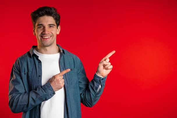 Happy smiling man presenting and showing something isolated on red background. Portrait of guy, he pointing with arms on his left with copy space. - Фото, зображення