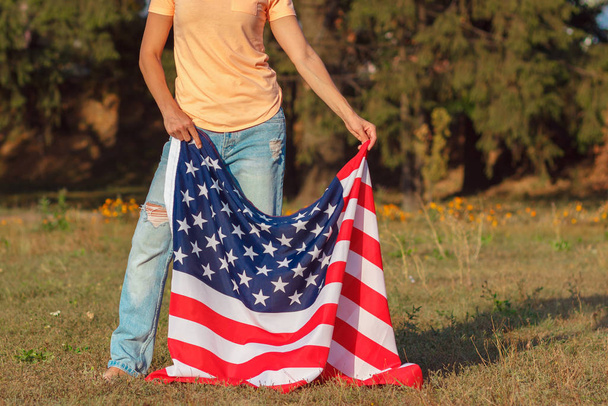 Mujer con una bandera de Estados Unidos de América en la mano, al aire libre, fondo de enfoque suave - Foto, imagen
