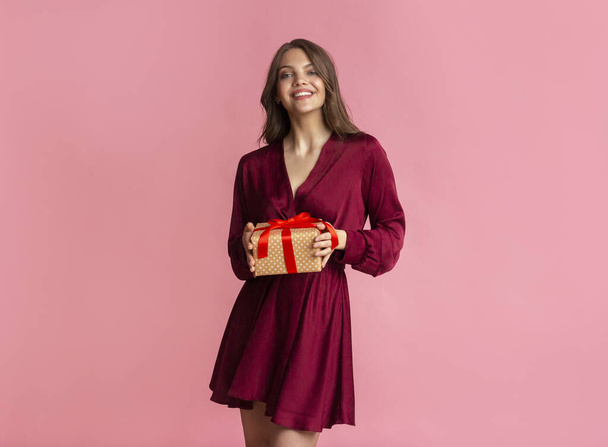 Радісна молода жінка тримає подарунок в руках і позує на камеру
 - Фото, зображення