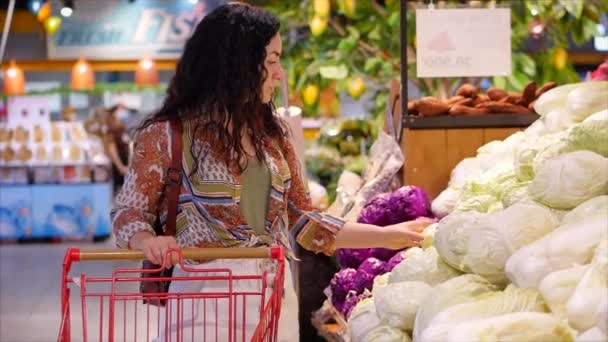 Pretty young girl or woman makes purchases in a supermarket buys food, healthy lifestyle, chooses healthy tomatoes, carrots, cabbage, lettuce, in the market, in the supermarket. Shopping. - Video