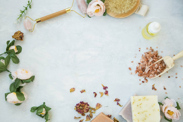 Spa still life frame with natural beauty products, bath salt, roses, natural soap, oil bottle, quartz face roller with copy space - 写真・画像