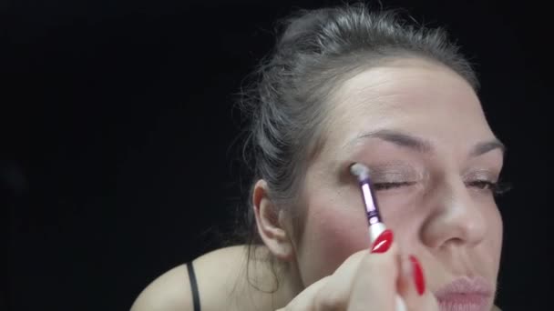 The girl makes her own makeup, looks after her face and creates beauty. Footage with makeup on a black background. - Πλάνα, βίντεο