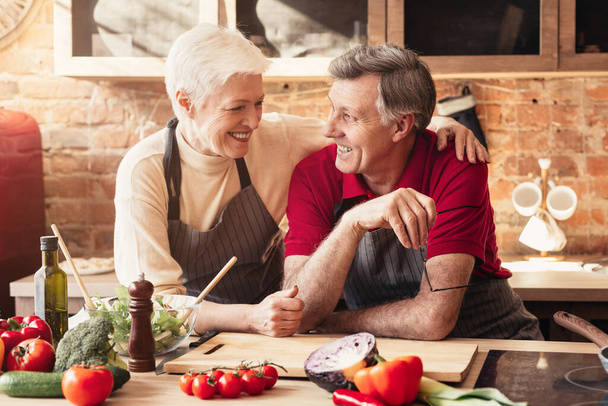 feliz casal de idosos abraçando na cozinha enquanto cozinhar o jantar juntos
 - Foto, Imagem