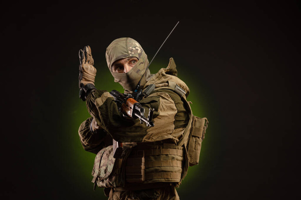 een saboteur soldaat in militaire kleding met een wapen op een donkere achtergrond toont gebaren - Foto, afbeelding