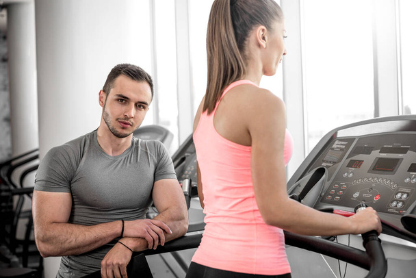 Personal fitness trainer watching his private client while walking on treadmill in modern fitness studio facility. - Φωτογραφία, εικόνα