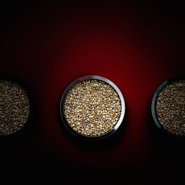 Hemp seeds in metal plates on a dark red background. Close up. - Fotografie, Obrázek
