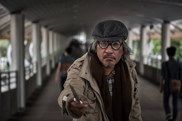 Homeless old man threaten by pointing knife to people at city sky walk. Poverty social issue and safety and danger life in town concept. Robbery and hostage in town. - 写真・画像