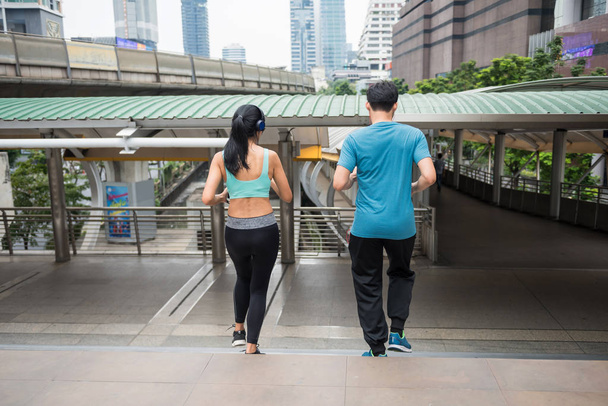 Rear of Asian couple jogging downstairs at modern city. people exercise cardio climbing staircase and listen stream online music from smartphone in town. Bodybuilding and healthy lifestyle. - Photo, Image