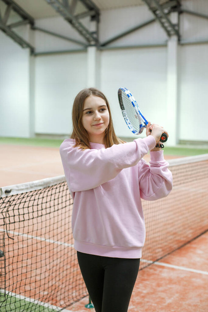 Een meisje met een tennisracket op een tennisbaan met kunstlicht kijkt naar de camera - Foto, afbeelding