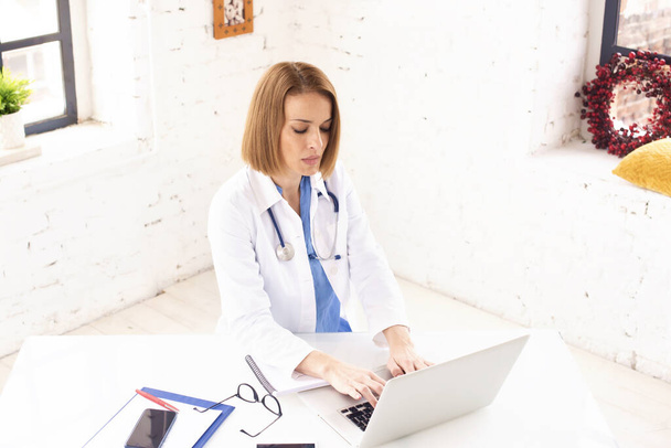 Shot of middle aged female doctor sitting behind her laptop and working.  - Photo, image