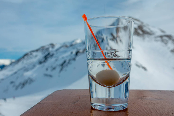 Auf einem Tisch steht ein Glas mit Alkohol und im Hintergrund die schneebedeckten Berge  - Foto, Bild