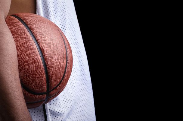Basketball player holding a ball against dark background - Zdjęcie, obraz