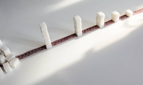 morceaux de sucre sur un ruban à mesurer un, deux, trois. Concept - Une consommation excessive de sucre entraîne l'obésité et le diabète
. - Photo, image