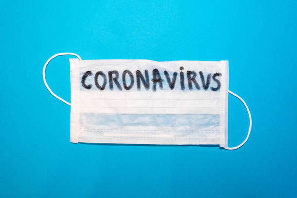 Coronavirus word written on a surgical medical mask. Wuhan , 2019-nCoV blue backgeound.  - Foto, afbeelding