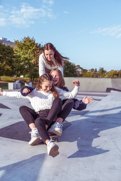 3 jeunes filles adolescentes écolières monter skateboard parc d'été. Vêtements décontractés pull jeans. Émotions bonheur, plaisir, détente, sourire rire, meilleures copines, repos après l'université
 - Photo, image