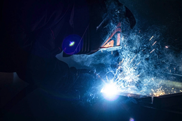 A masked welder in full darkness welds a metal. - Foto, imagen