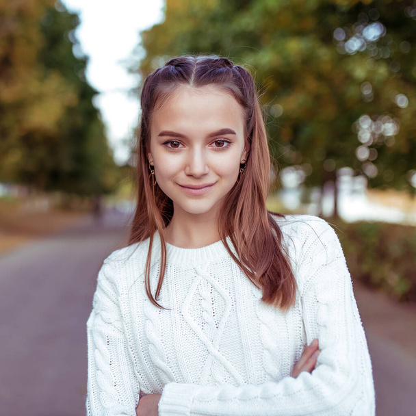 Detailní portrét dívky, dospívající školačky, v bílém pleteném svetru, v létě v parku. Šťastné úsměvy, emoce pozitivní a radostné. Dlouhé vlasy. Odpočinek po škole, stromy na pozadí. - Fotografie, Obrázek
