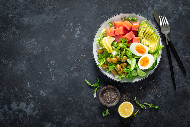 Ketogenic, paleo diet lunch bowl with salted salmon fish, lemon, avocado, olives, boiled egg, cucumber, green lettuce salad and chia seeds, healthy food trend, top view - Фото, зображення