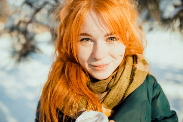 Portraits of a charming red-haired girl with a cute face. Girl posing on camera in the city center in winter. She has a wonderful mood and a lovely smile. - Photo, Image