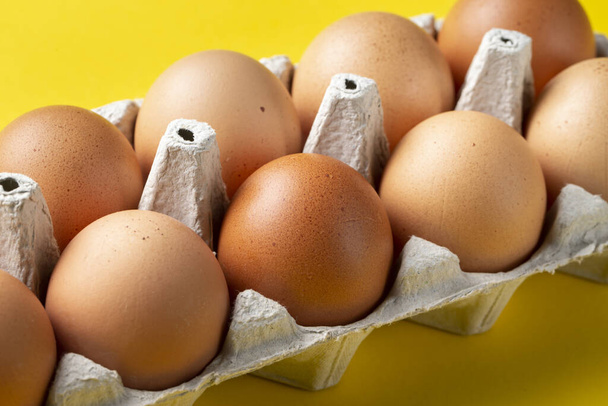 Brown eggs in box on yellow background. - Zdjęcie, obraz