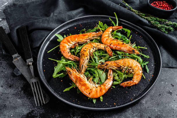 Salad with grilled giant langoustine shrimp, prawns and arugula. Black background. Top view. - Photo, Image