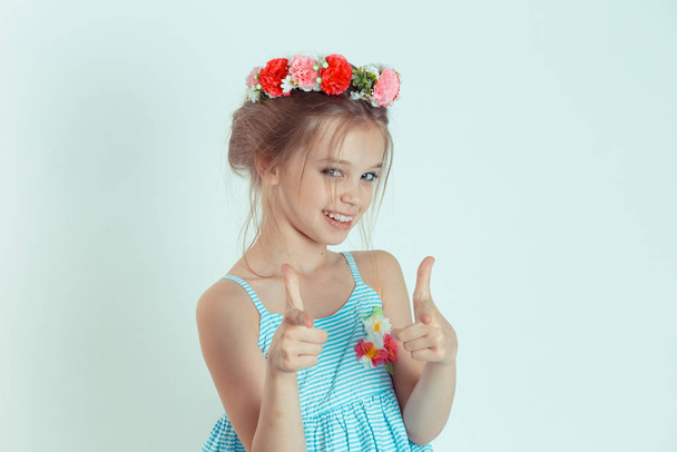 Hey you! Cute kid pretty girl pointing at camera, point index fingers hands like guns gesture. Closeup portrait of Caucasian kid model with floral headband isolated on white blue copy space background - Photo, Image