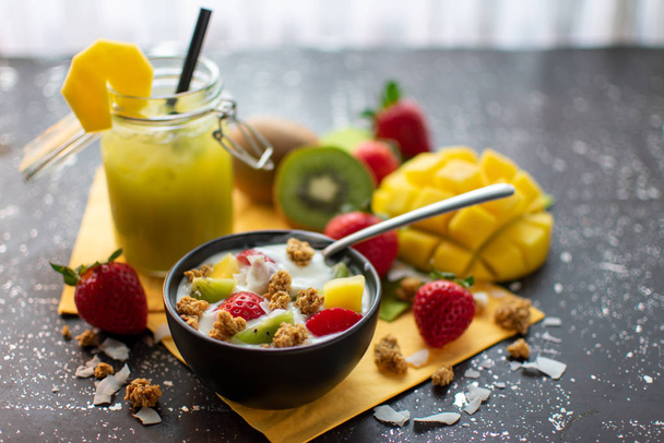 healthy breakfast: crispy muesli with yoghurt fresh strawberries, kiwis, mangoes, coconut flakes and spoon  - Foto, afbeelding