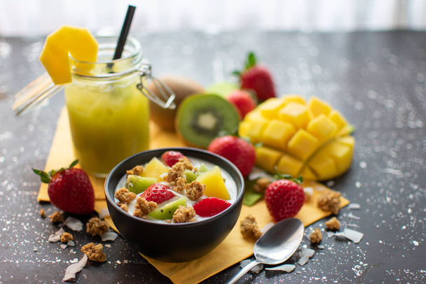 healthy breakfast: yoghurt with crunchies, fresh strawberries, kiwis, mangoes and coconut flakes with. accompanied by a smoothie with mango slice - Fotó, kép