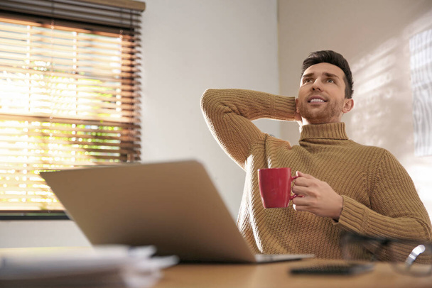 Young man with cup of drink relaxing at workplace - Photo, Image