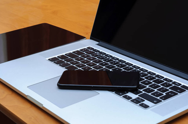Blick auf einen Laptop-PC und ein Smartphone und ein Tablet auf einem Schreibtisch im Homeoffice-Umfeld im Wohnzimmer. - Foto, Bild