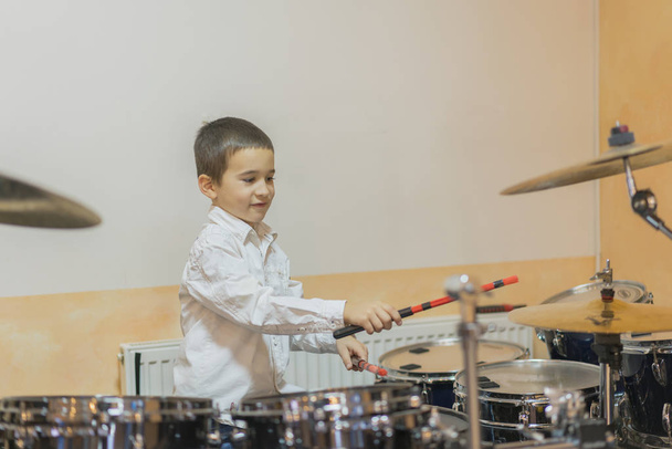 Хлопчик барабани. хлопчик у білій сорочці грає на барабанах. Хлопчик у білій сорочці б'є
. - Фото, зображення