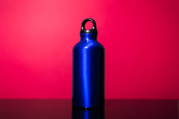 ピンクのサンゴの背景に隔離されたアルミニウム熱環境水ボトルの古典的な青. - 写真・画像