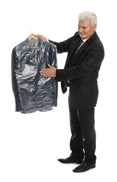 Senior man holding hanger with jacket in plastic bag on white background. Dry-cleaning service - Foto, Imagem