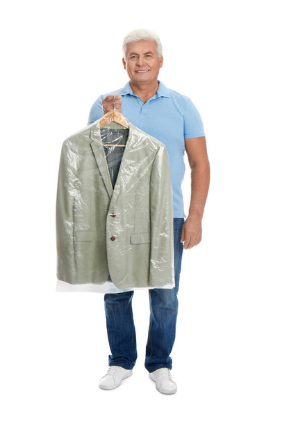 Senior man holding hanger with jacket in plastic bag on white background. Dry-cleaning service - Фото, изображение
