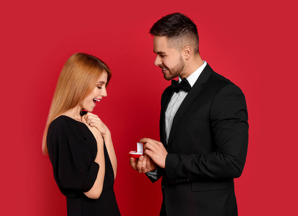 Man with engagement ring making marriage proposal to girlfriend on red background - Фото, зображення