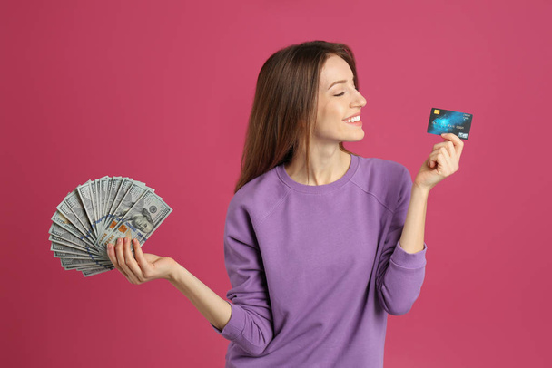 Happy young woman with cash money and credit card on pink background - Foto, imagen