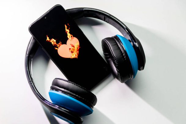 Il simbolo del cuore ardente con fiamme ardenti sullo schermo di uno smartphone nero e cuffie blu sopra le cuffie e lo spazio di copia mostra l'amore per la musica e i servizi di streaming musicale
 - Foto, immagini