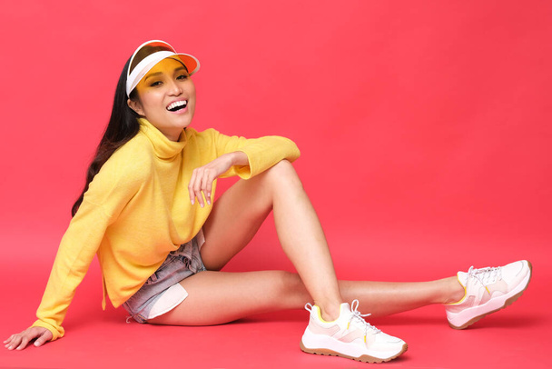 Sonriente modelo asiático con ropa de colores. Jersey amarillo sobre fondo rojo
. - Foto, imagen