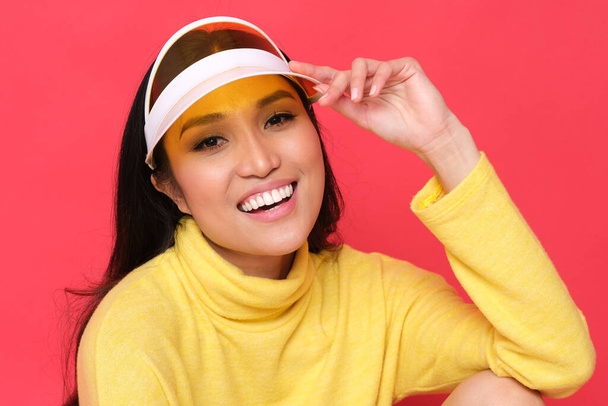 Lachend Aziatisch model met kleurrijke kleren. Gele trui op rode achtergrond. - Foto, afbeelding