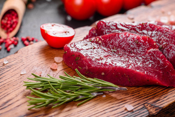 Fresh Raw Beef steak Mignon, with salt, peppercorns, thyme, tomatoes. Raw fresh marbled meat Steak and seasonings on a dark background - Photo, Image