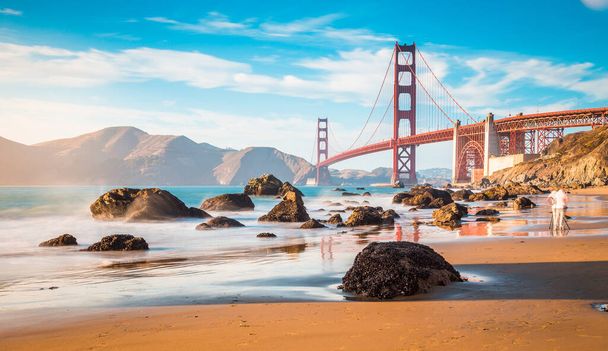 Klasyczny widok panoramiczny słynnego mostu Golden Gate widziany z malowniczej plaży Baker w pięknym złotym wieczornym świetle w słoneczny dzień z błękitnym niebem i chmurami w lecie, San Francisco, Kalifornia, USA - Zdjęcie, obraz