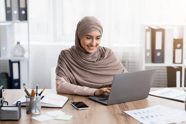 Joven mujer de negocios musulmana trabajando en su computadora portátil en la oficina
 - Foto, imagen