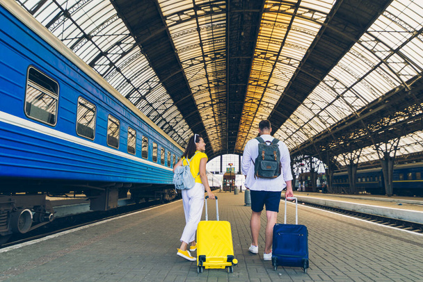 νεαρό ζευγάρι με τα πόδια από το σιδηροδρομικό σταθμό με βαλίτσες σε τροχούς έννοια ταξιδιού - Φωτογραφία, εικόνα